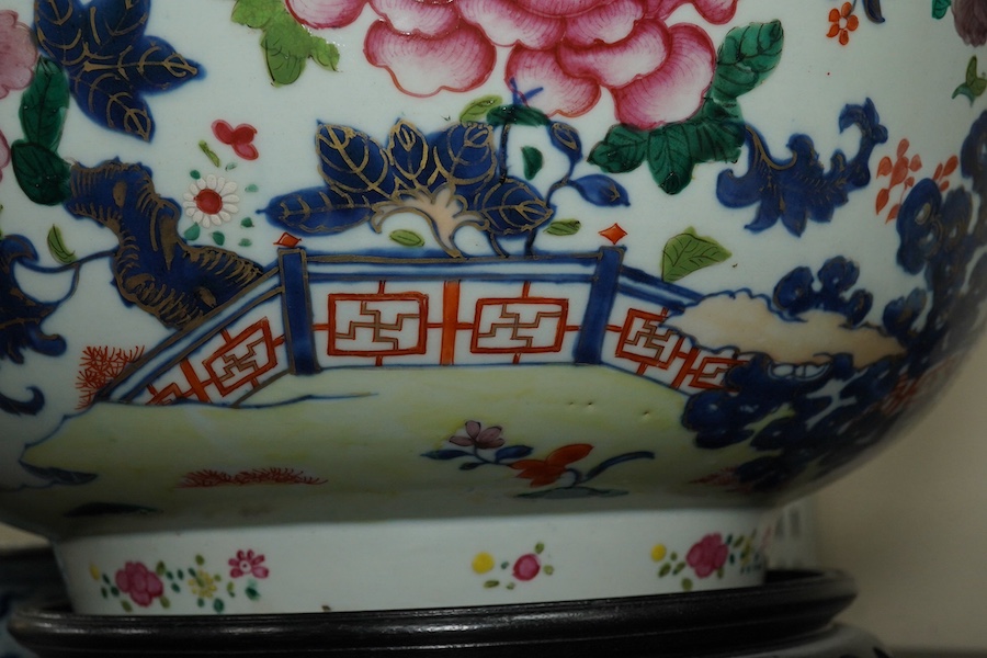 A large Chinese famille rose punch bowl, Qianlong period, the exterior painted with flowers in a fenced garden, the interior with a flower bouquet within a garland of flowers, 40.5cm diameter, wood stand. Condition - som